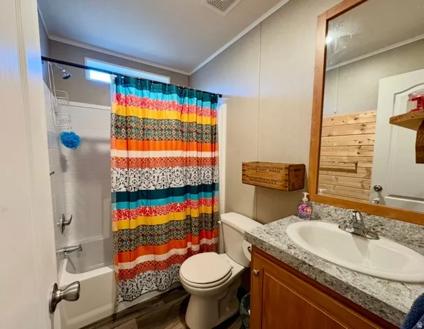 Full bathroom featuring vanity, shower / tub combo with curtain, crown molding, and dark wood-type flooring