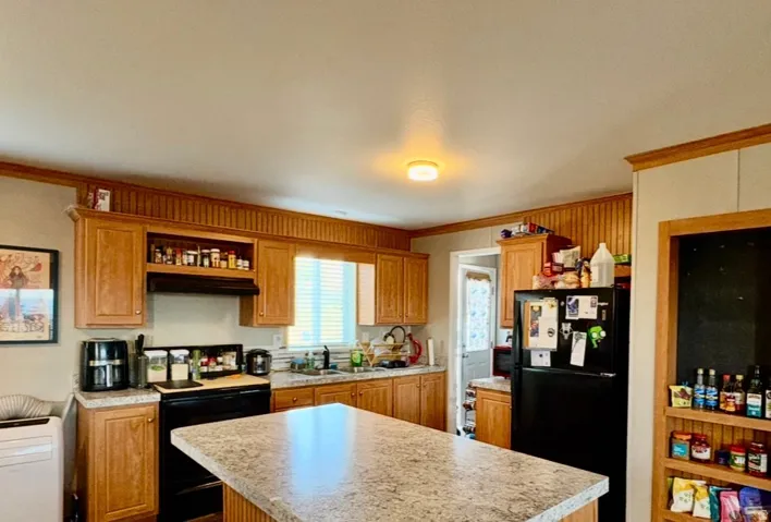 Kitchen featuring black appliances, a kitchen island, light countertops, ornamental molding, and wood finish cabinetry