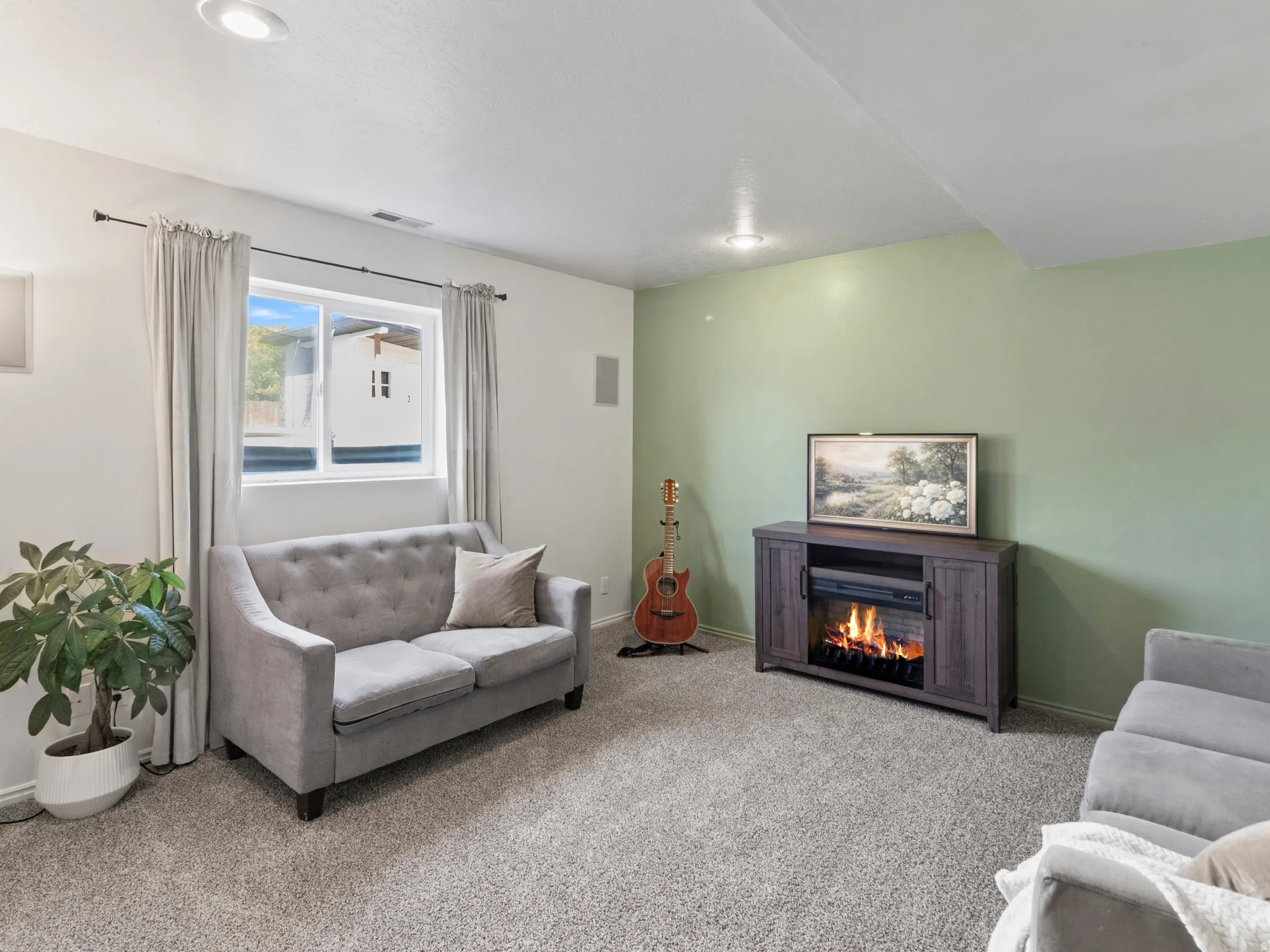 Living area with light colored carpet and a lit fireplace