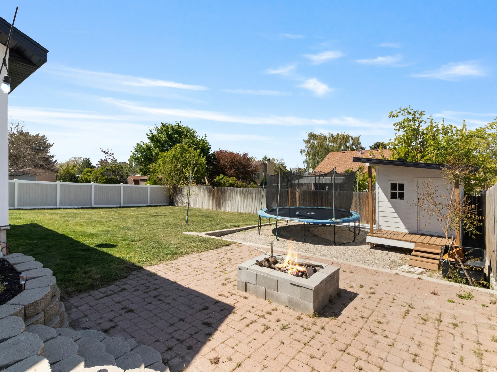 Fenced backyard featuring a storage shed, a trampoline, a fire pit, a patio, and a wooden deck