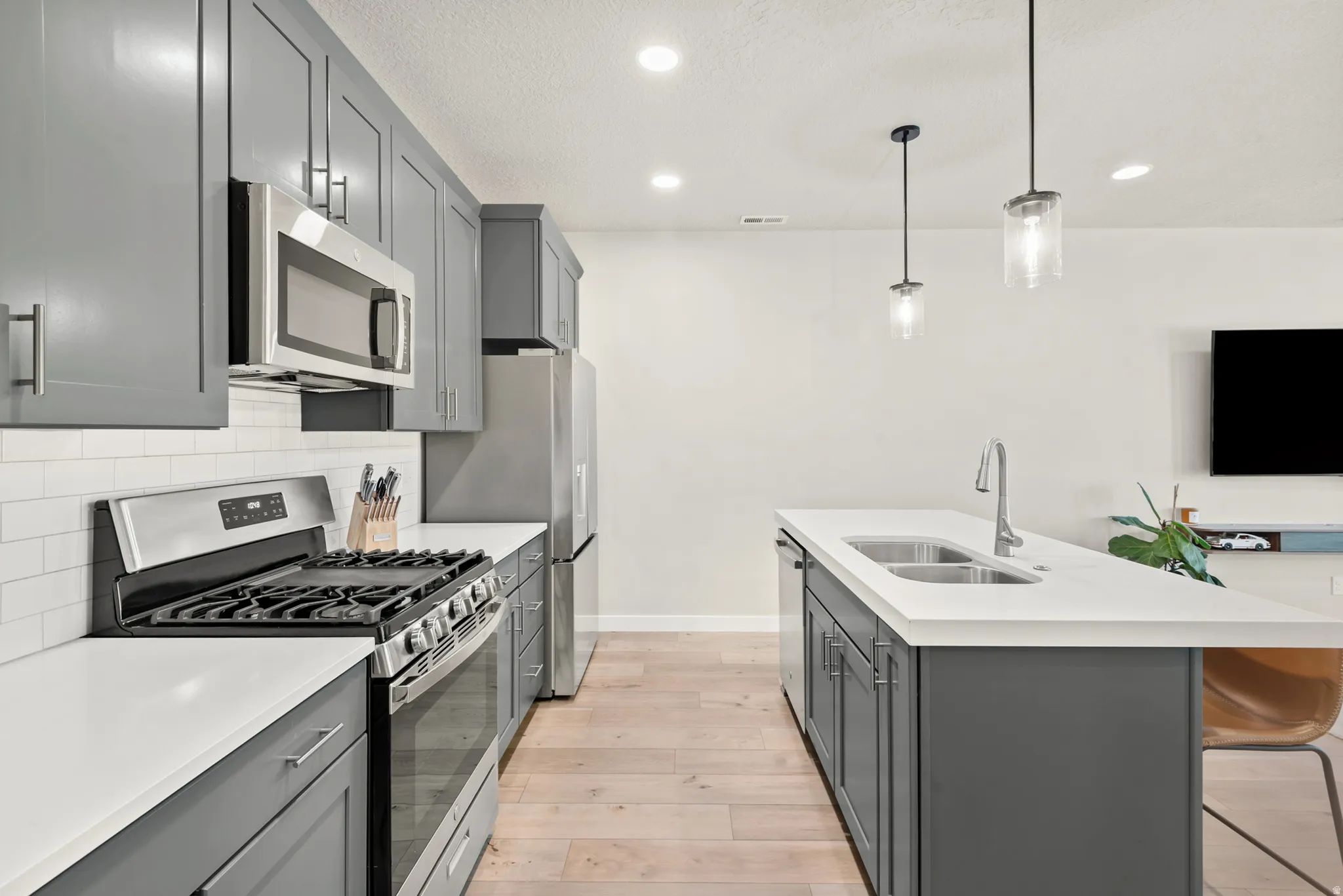 Modern kitchen featuring gray shaker-style cabinetry, stainless steel appliances, white countertops, and a subway tile backsplash