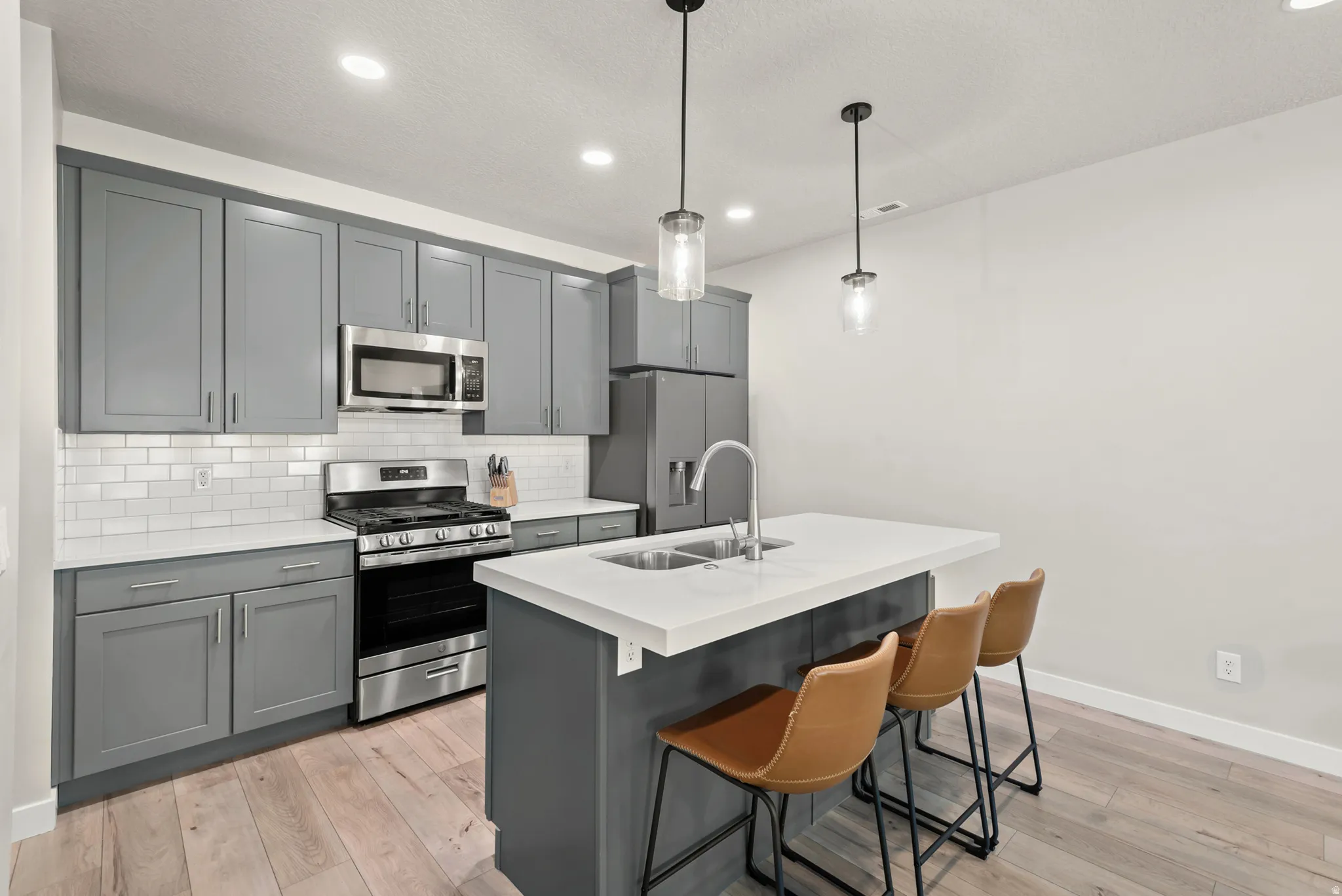 Contemporary kitchen featuring grey cabinetry, stainless steel appliances, white subway tile backsplash, and light wood-finish flooring