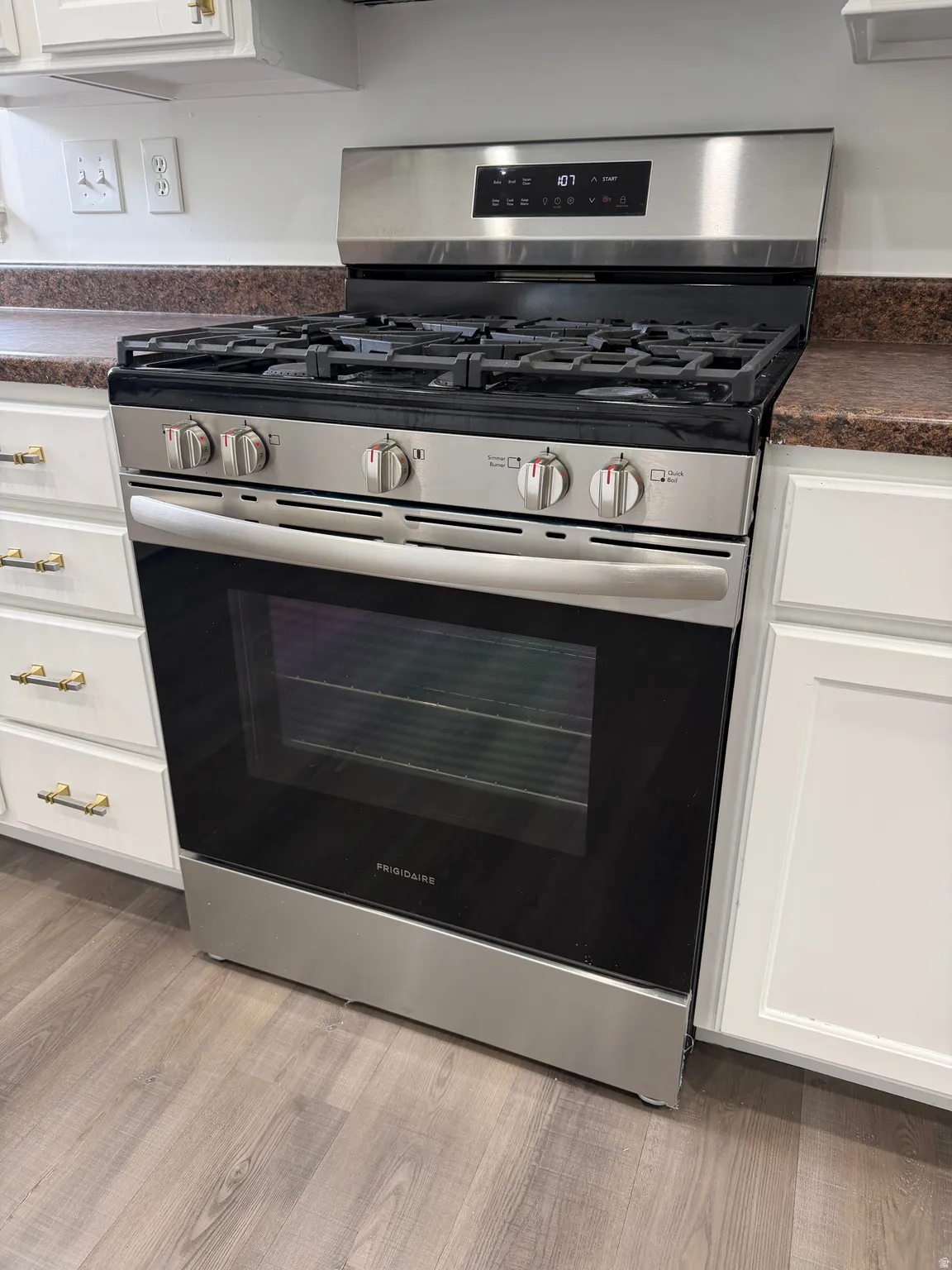 Kitchen view of dark countertops, white cabinets, stainless steel gas stove, and light wood finished floors
