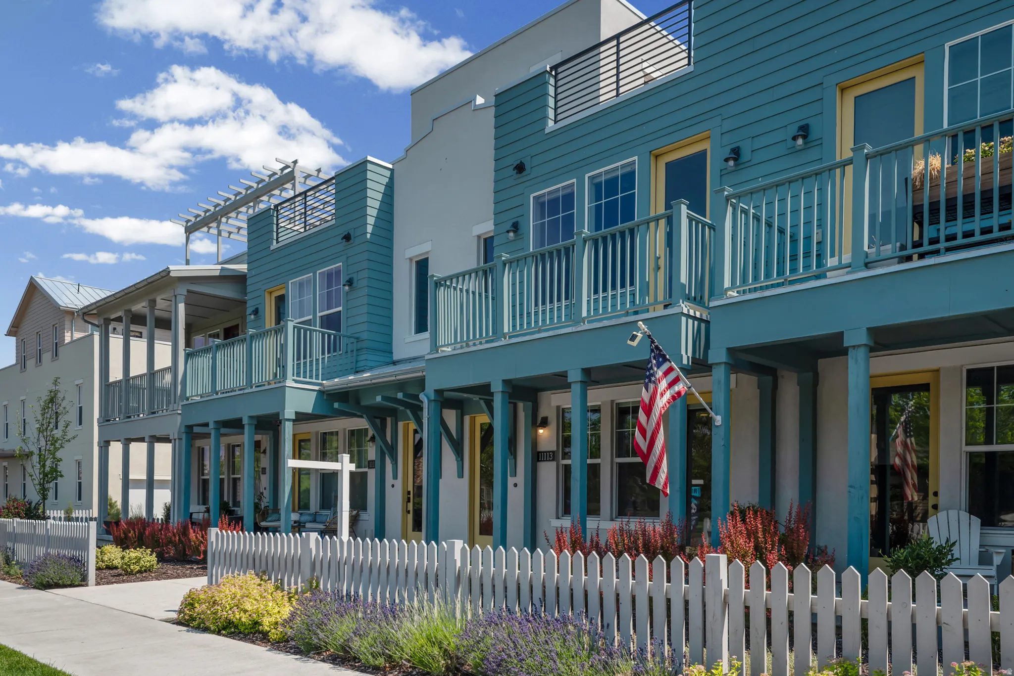Two-story townhome featuring a blue exterior with contrasting yellow trim, a white picket fence, and a landscaped front yard