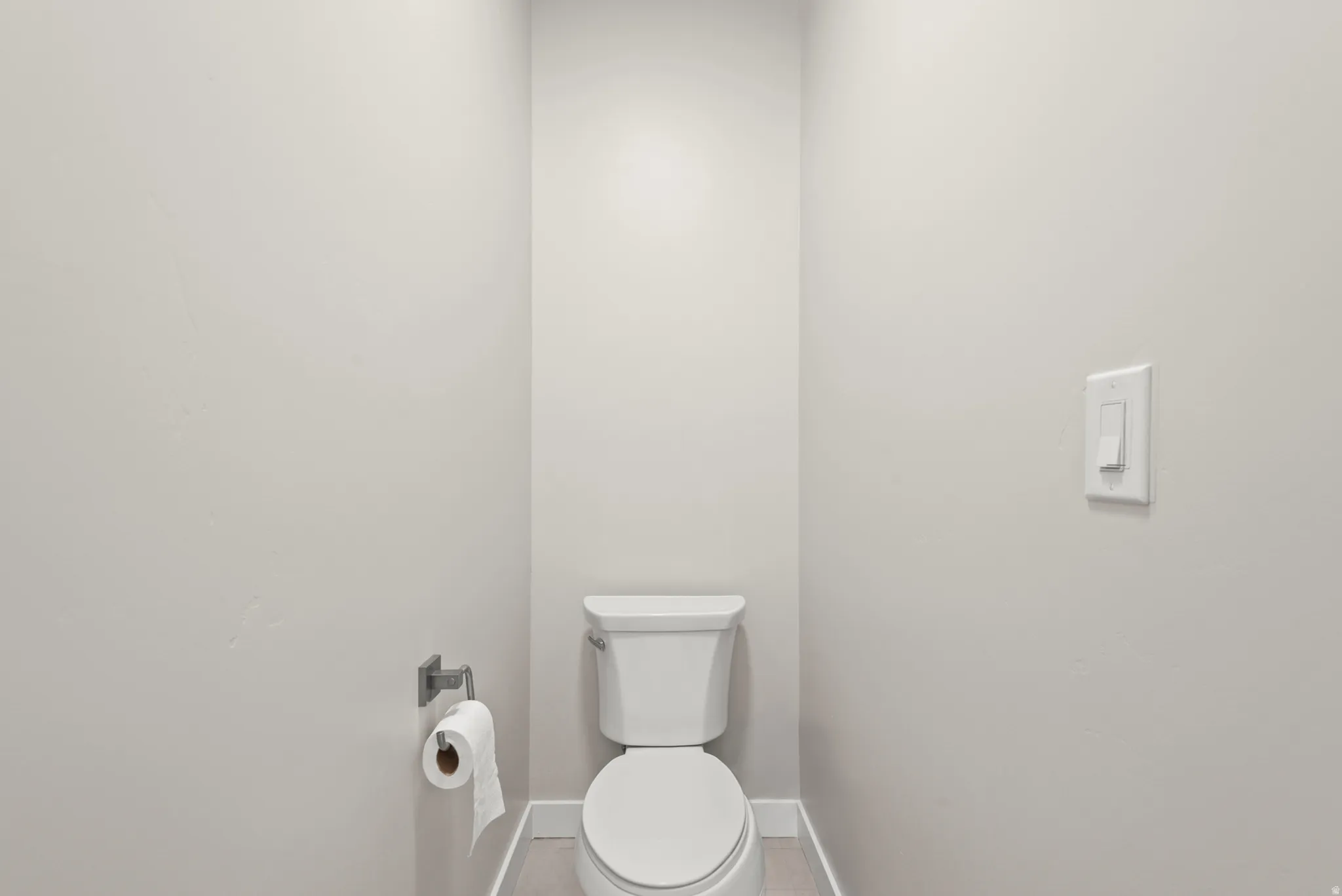 Powder room featuring a white toilet, light gray walls, and light wood-finish flooring