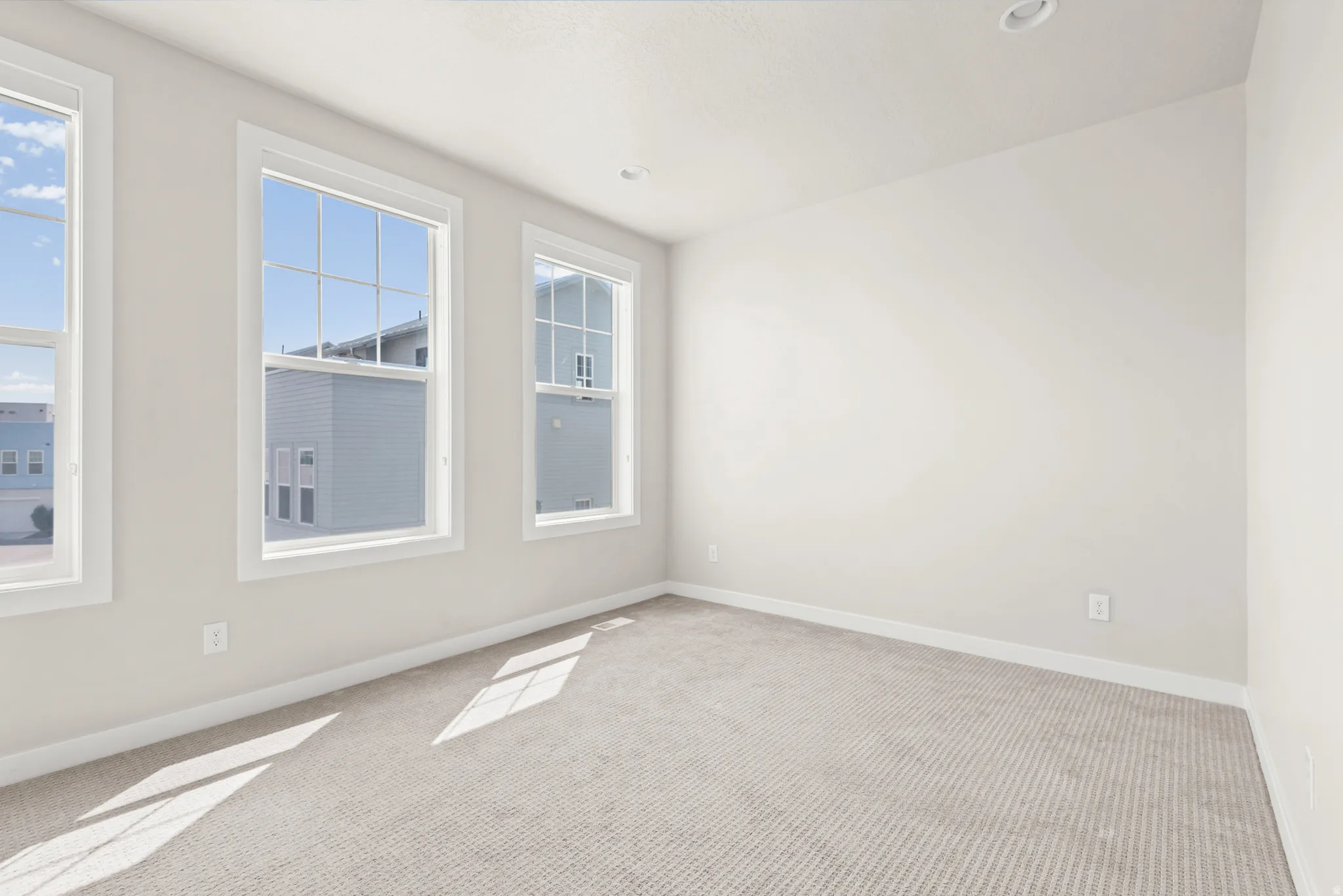 Room featuring three windows with white frames, neutral wall paint, recessed lighting, and light-colored carpeting