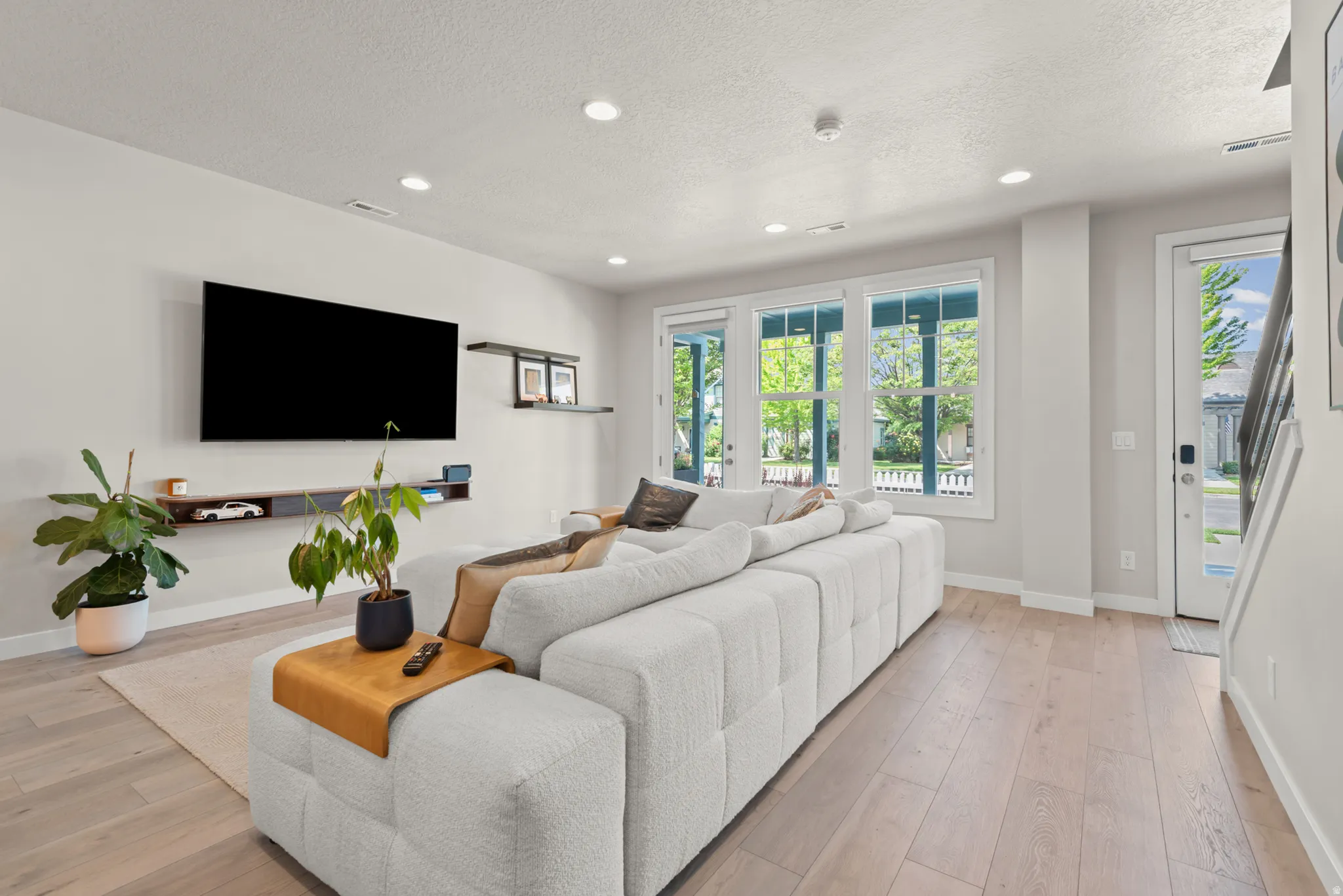 Bright living space featuring light wood-finish flooring, recessed lighting, and a wall-mounted media console