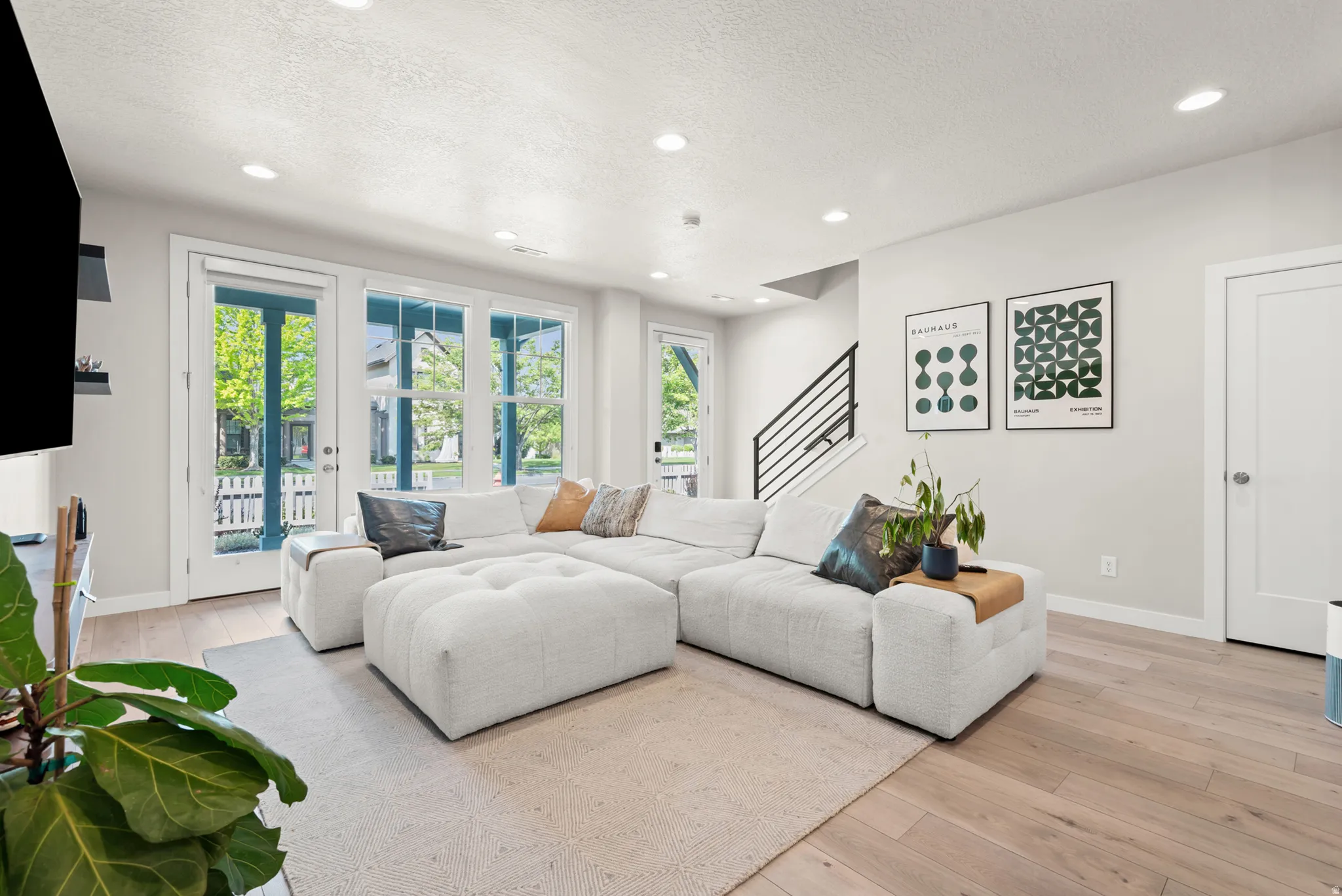 Spacious living area featuring light wood-finish flooring, recessed lighting, and ample natural light through multiple full-lite patio doors