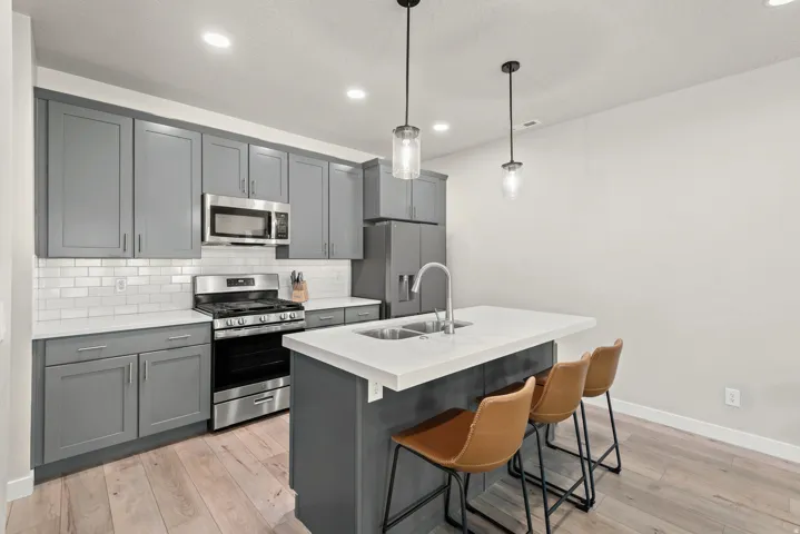 Contemporary kitchen featuring grey cabinetry, stainless steel appliances, white subway tile backsplash, and light wood-finish flooring