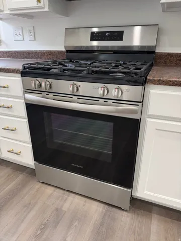 Kitchen view of dark countertops, white cabinets, stainless steel gas stove, and light wood finished floors