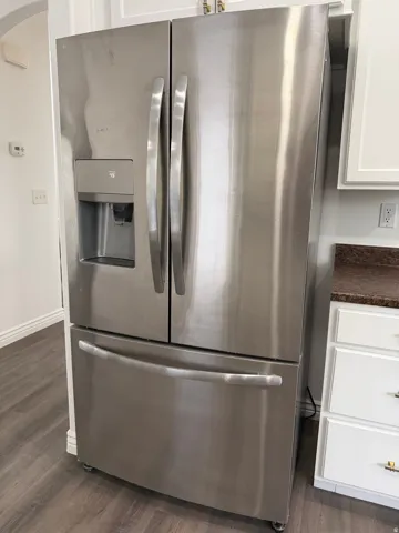 Kitchen view of stainless steel fridge with ice dispenser, dark countertops, white cabinets, and dark wood-style floors