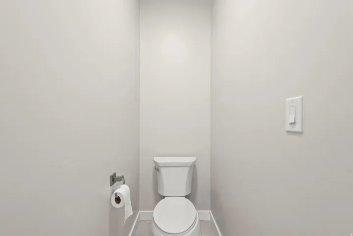 Powder room featuring a white toilet, light gray walls, and light wood-finish flooring