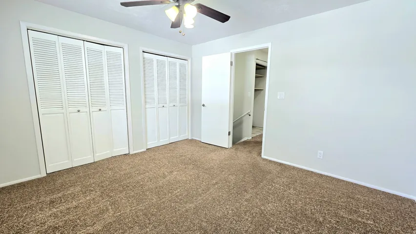 Unfurnished bedroom featuring multiple closets, dark carpet, and ceiling fan