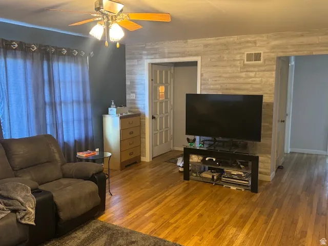 Living area featuring hardwood / wood-style flooring, ceiling fan, and wood walls