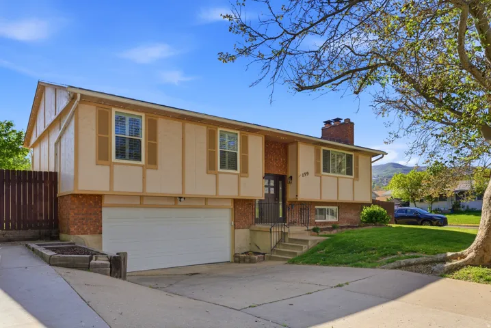 Split foyer home featuring an attached garage, brick siding, a chimney, concrete driveway, and a front yard