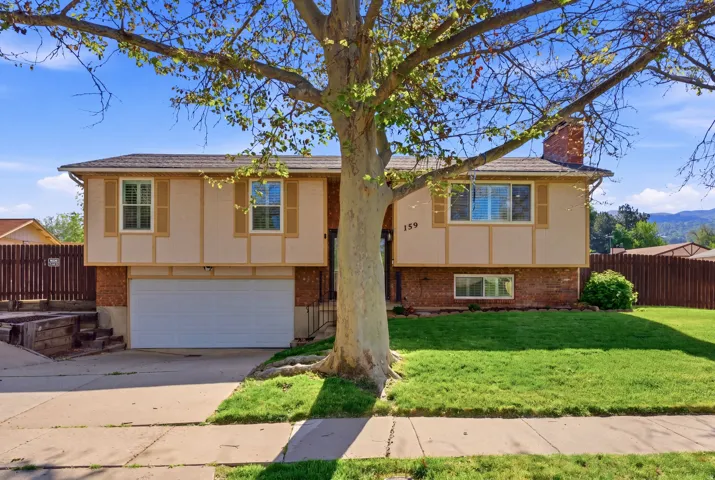 Split foyer home with brick siding, concrete driveway, a chimney, a garage, and stucco siding