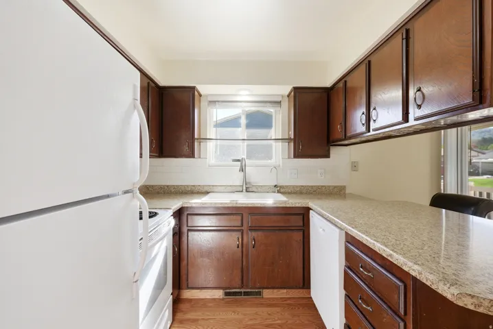 Kitchen with white appliances, light countertops, dark wood finish cabinets, light wood-type flooring, and decorative backsplash