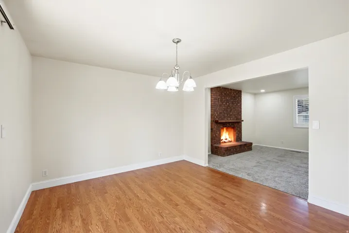 Unfurnished dining area with a brick fireplace, light wood finished floors, and a chandelier