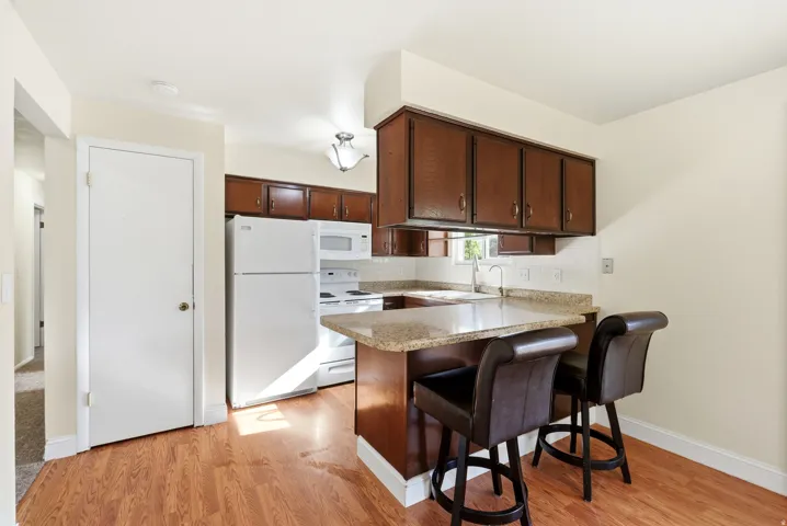 Kitchen featuring white appliances, a peninsula, a breakfast bar area, and light wood-type flooring