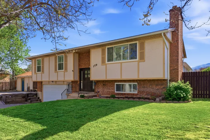 Raised ranch featuring a chimney, brick siding, an attached garage, and stucco siding