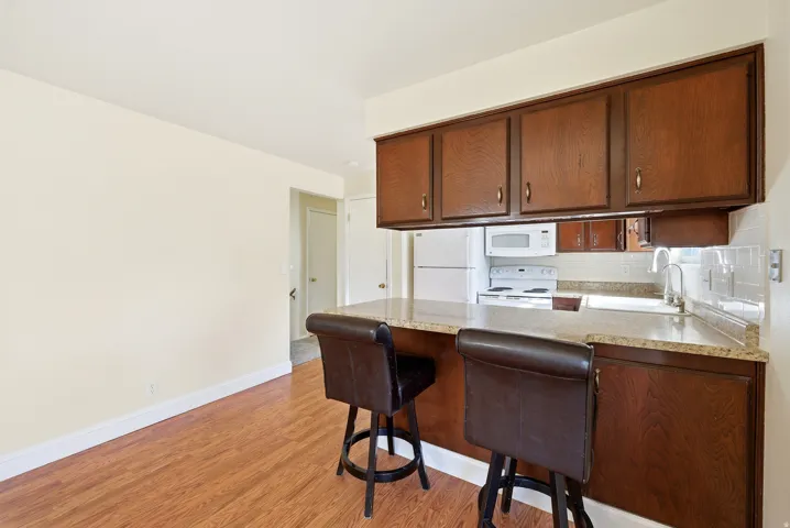 Kitchen featuring a peninsula, light countertops, white appliances, light wood-type flooring, and a breakfast bar