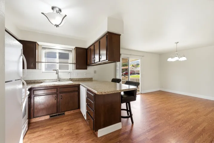 Kitchen featuring a kitchen breakfast bar, a peninsula, dark wood finish cabinets, white appliances, and tasteful backsplash