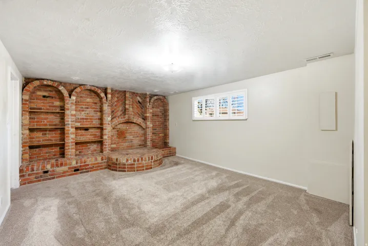 Unfurnished living room featuring brick wall, carpet flooring, and a textured ceiling