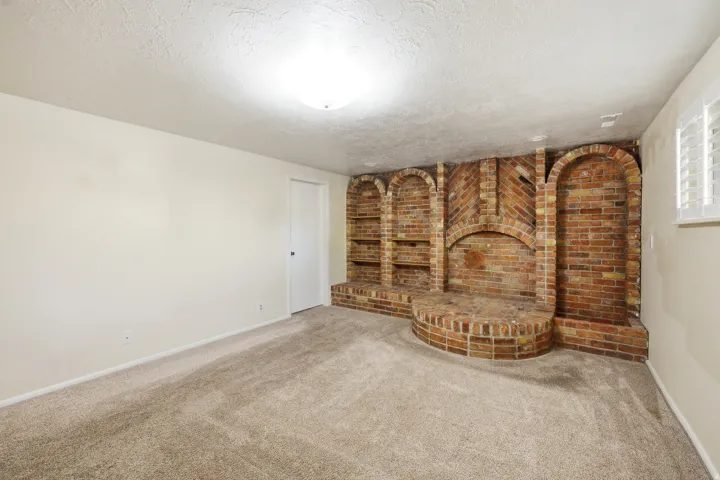 Unfurnished living room with brick wall, carpet flooring, and a textured ceiling