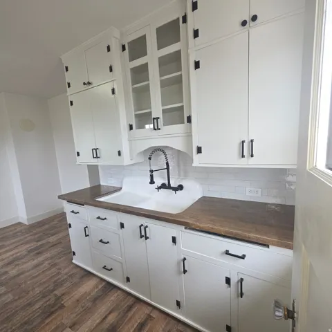 Kitchen with white cabinets, dark wood-type flooring, backsplash, and glass insert cabinets