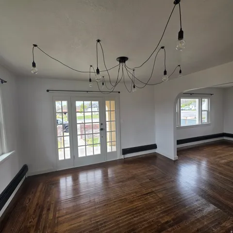Unfurnished dining area featuring arched walkways, dark wood-type flooring, a baseboard heating unit, and hanging lights