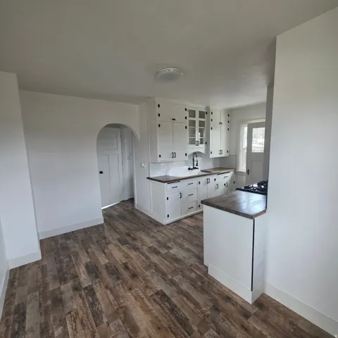 Kitchen featuring white cabinets, arched walkways, dark countertops, dark wood-style floors, and glass insert cabinets