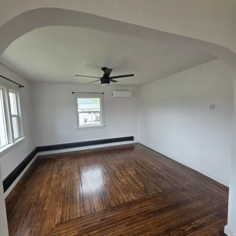 Spare room featuring arched walkways, dark wood finished floors, a ceiling fan, and a baseboard radiator