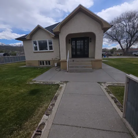 Property entrance with stucco siding, a lawn, and covered porch