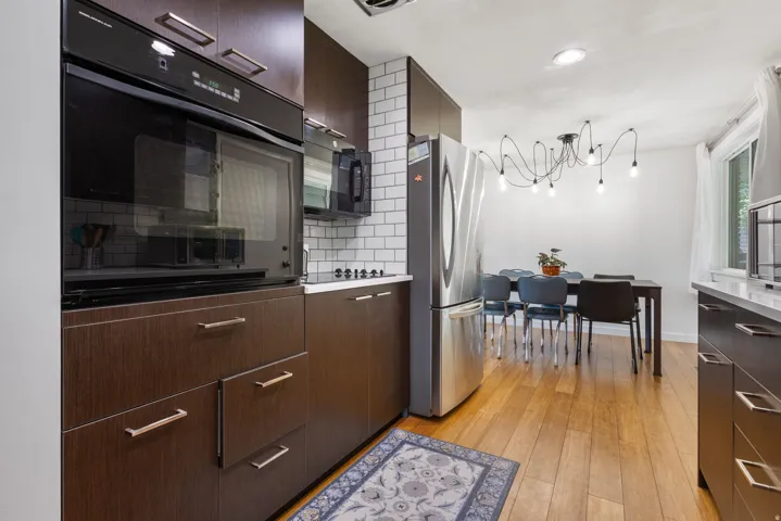 Kitchen with black appliances, dark wood finish cabinetry, light wood-type flooring, suspended lighting, and modern cabinets