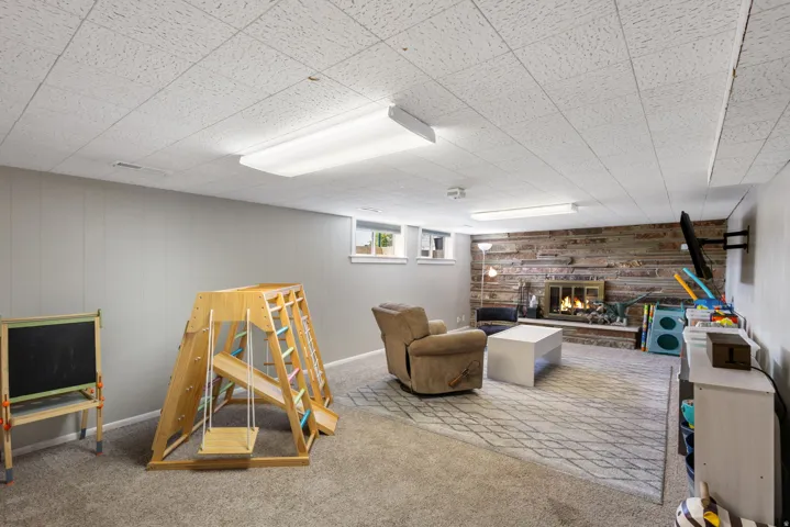 Game room with a brick fireplace, wooden walls, and carpet flooring