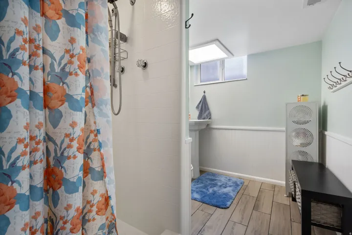 Bathroom with wainscoting, tiled shower, and wood finish floors