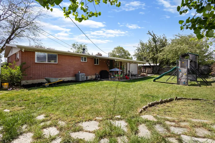 Back of house with brick siding, a patio area, a playground, and a chimney