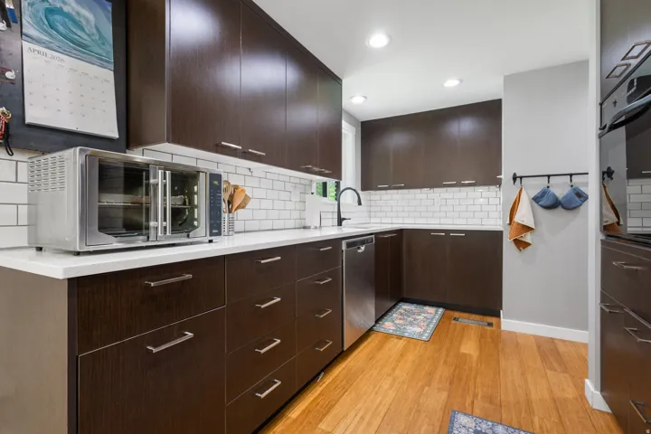 Kitchen featuring dark wood finish cabinets, light wood-type flooring, stainless steel appliances, decorative backsplash, and recessed lighting