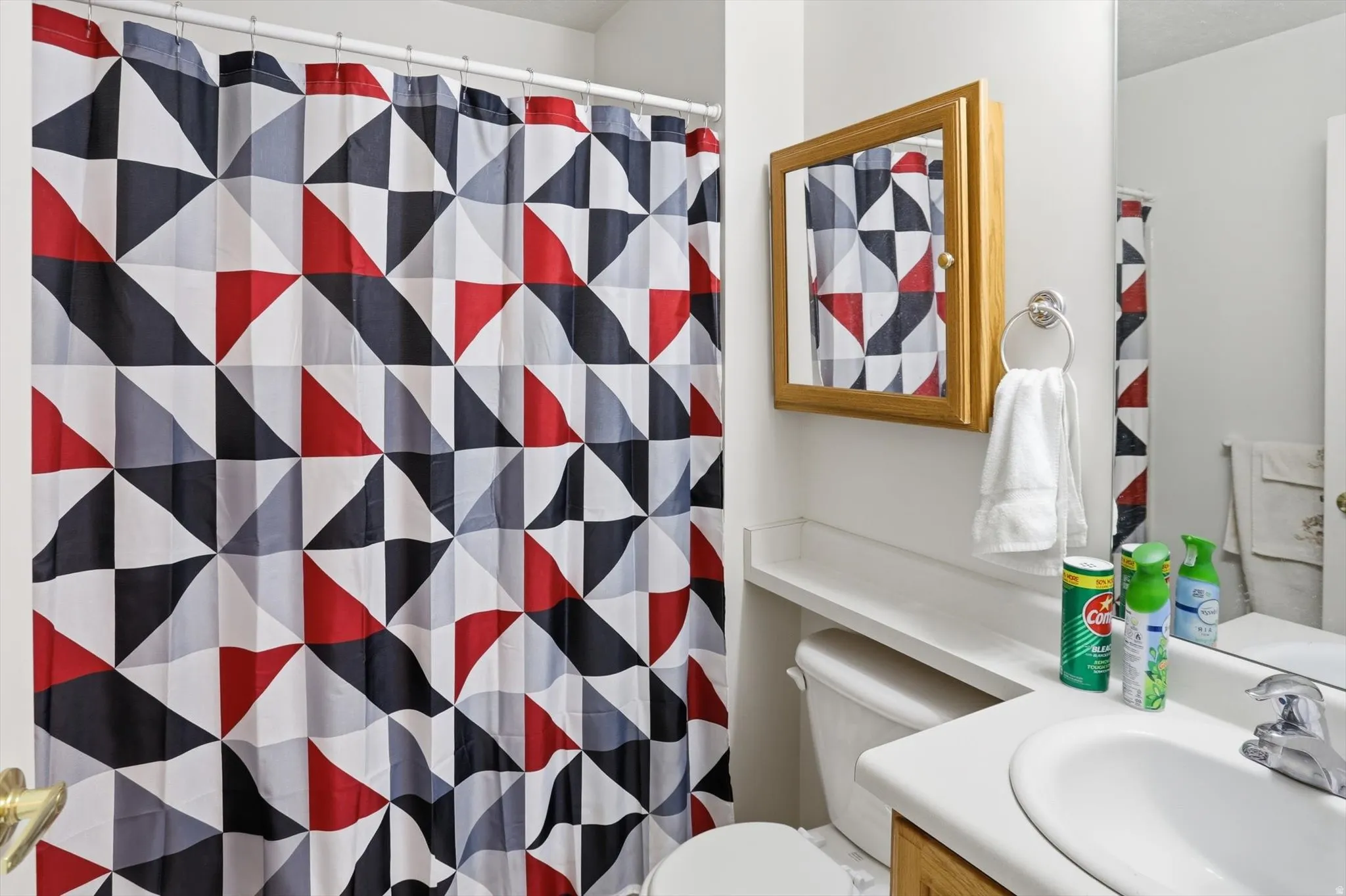 Bathroom featuring a built-in wood-frame medicine cabinet, an integrated white sink, a chrome faucet, a towel ring, and a white toilet