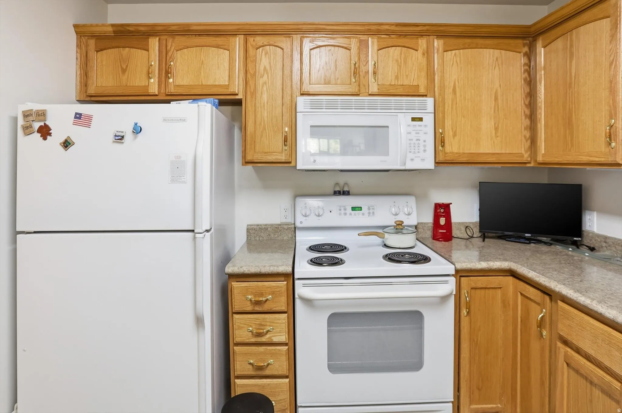 Kitchen featuring light wood cabinetry with decorative arch panels, white appliances, and speckled countertops