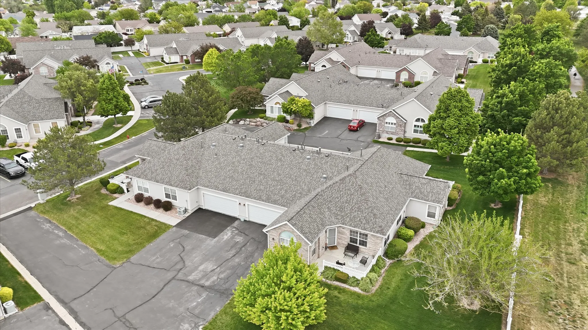 Multi-unit residential structure featuring attached garages, individual patios, mature landscaping, and an asphalt driveway