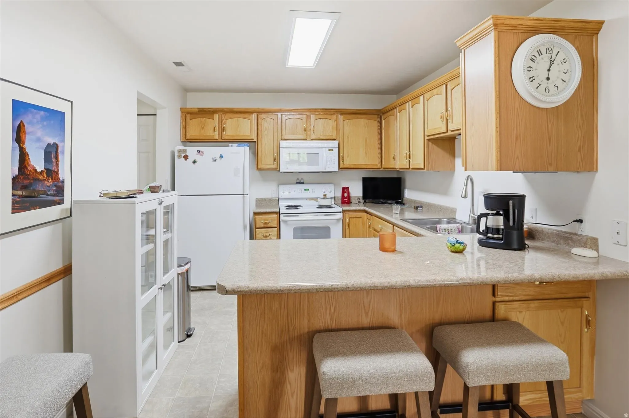 Kitchen featuring wood cabinetry, solid surface countertops, white appliances, and a breakfast bar with seating