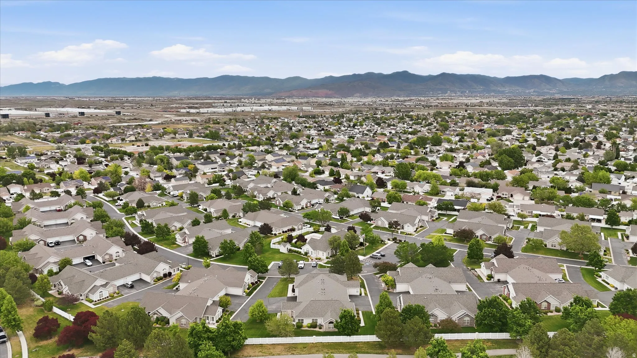 Extensive residential development featuring numerous single-story homes, mature landscaping, and curved streets, with distant mountains forming a natural backdrop