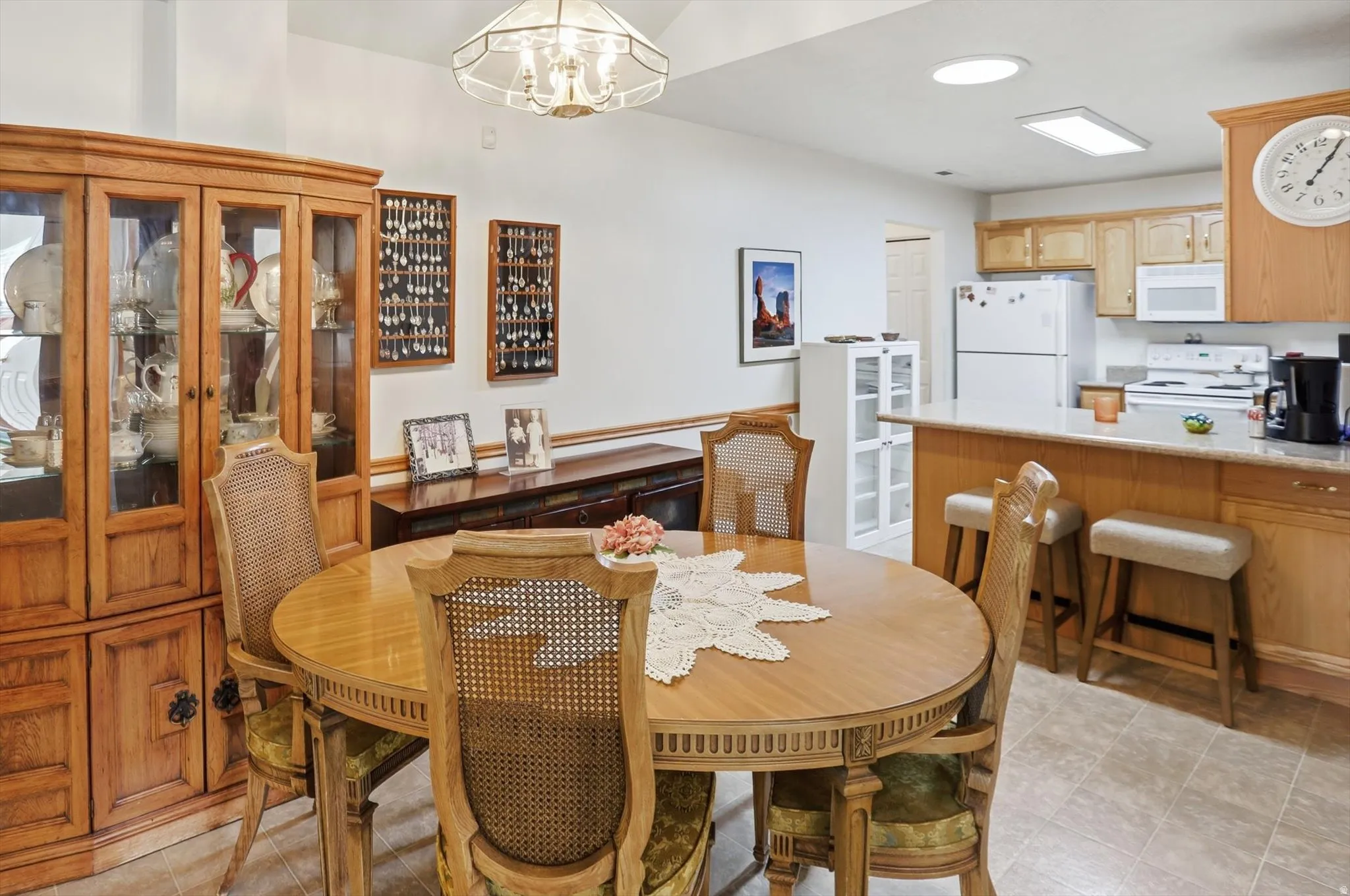 Open-concept dining area featuring a built-in breakfast bar with seating, light wood cabinetry, and a full suite of white appliances