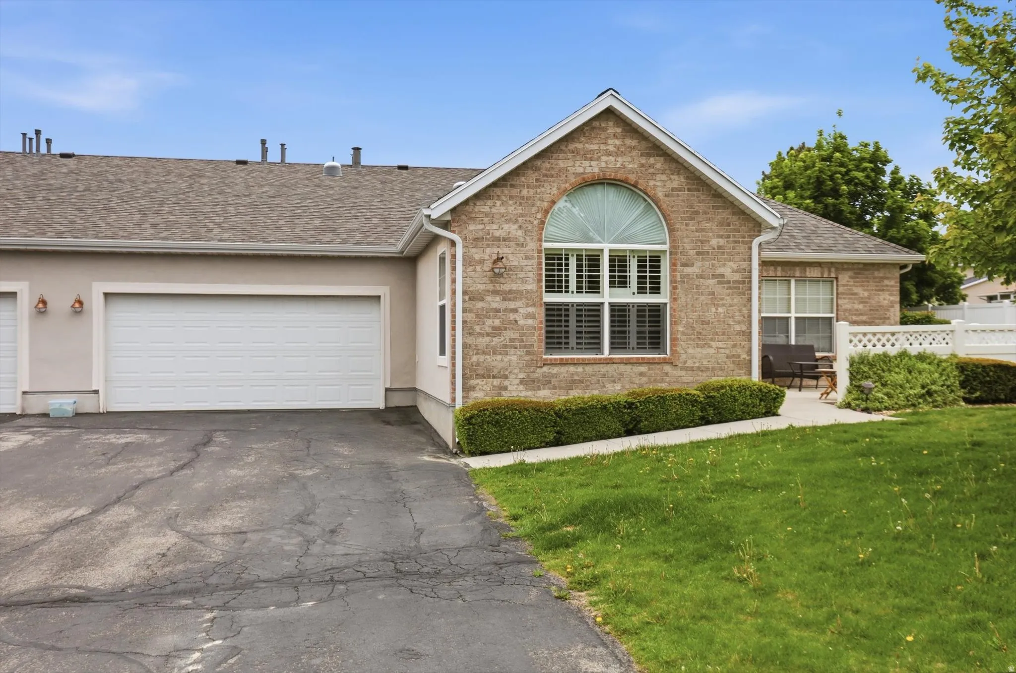 Brick and stucco exterior featuring an arched window, a two-car garage, and a covered entryway