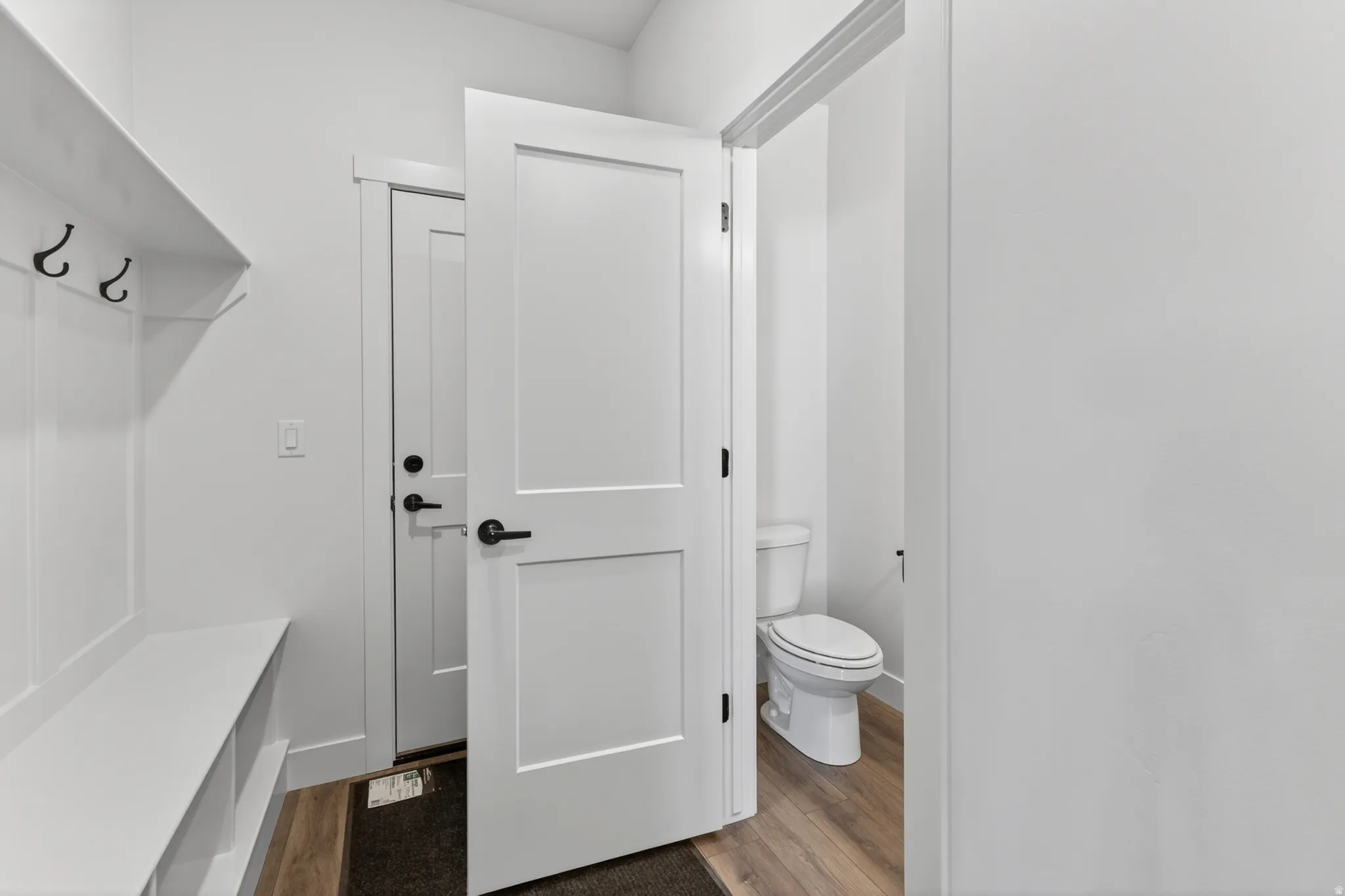 Entryway mudroom featuring a built-in bench with storage cubbies and coat hooks, wood-finish flooring, and a flat-panel interior door with matte black hardware