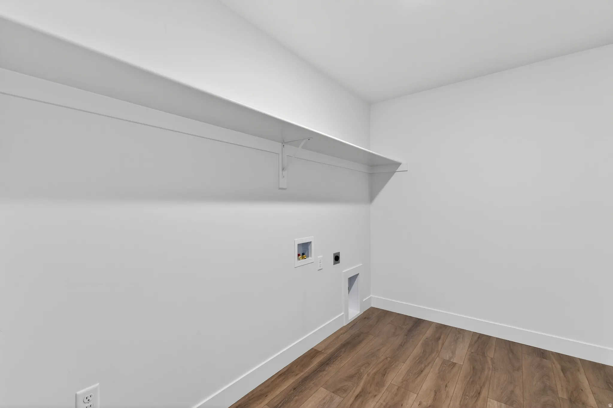 Dedicated utility room featuring wood-finish flooring, white walls, and a built-in wall shelf