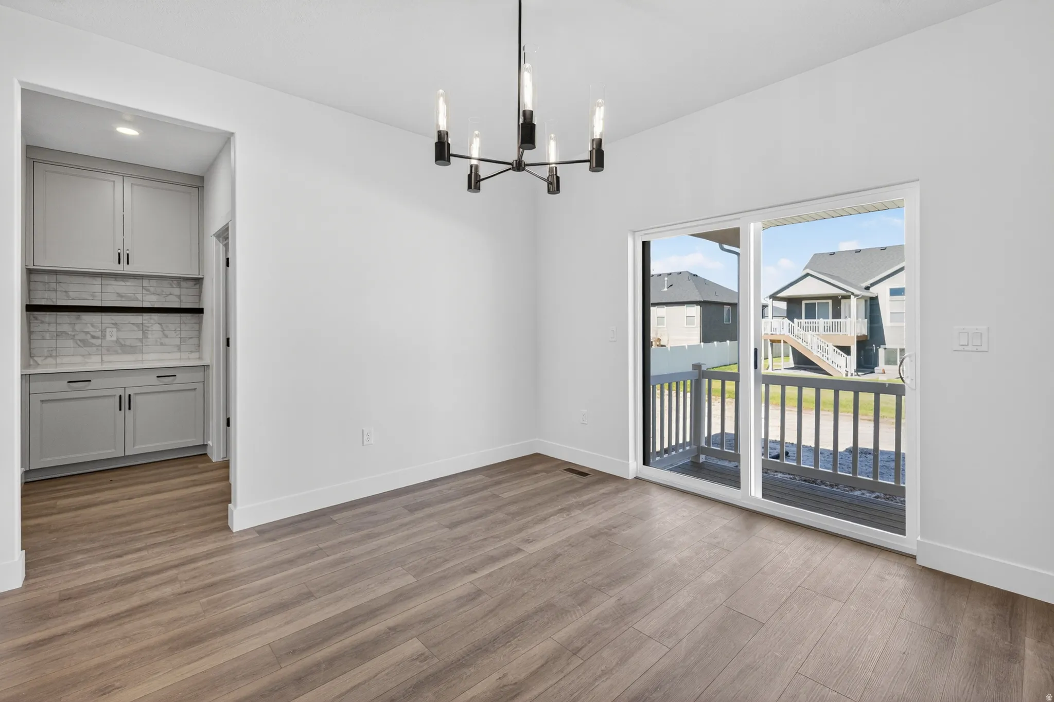 Wood-finish flooring throughout, featuring a modern chandelier, sliding glass door with deck access, and built-in cabinetry with a tiled backsplash