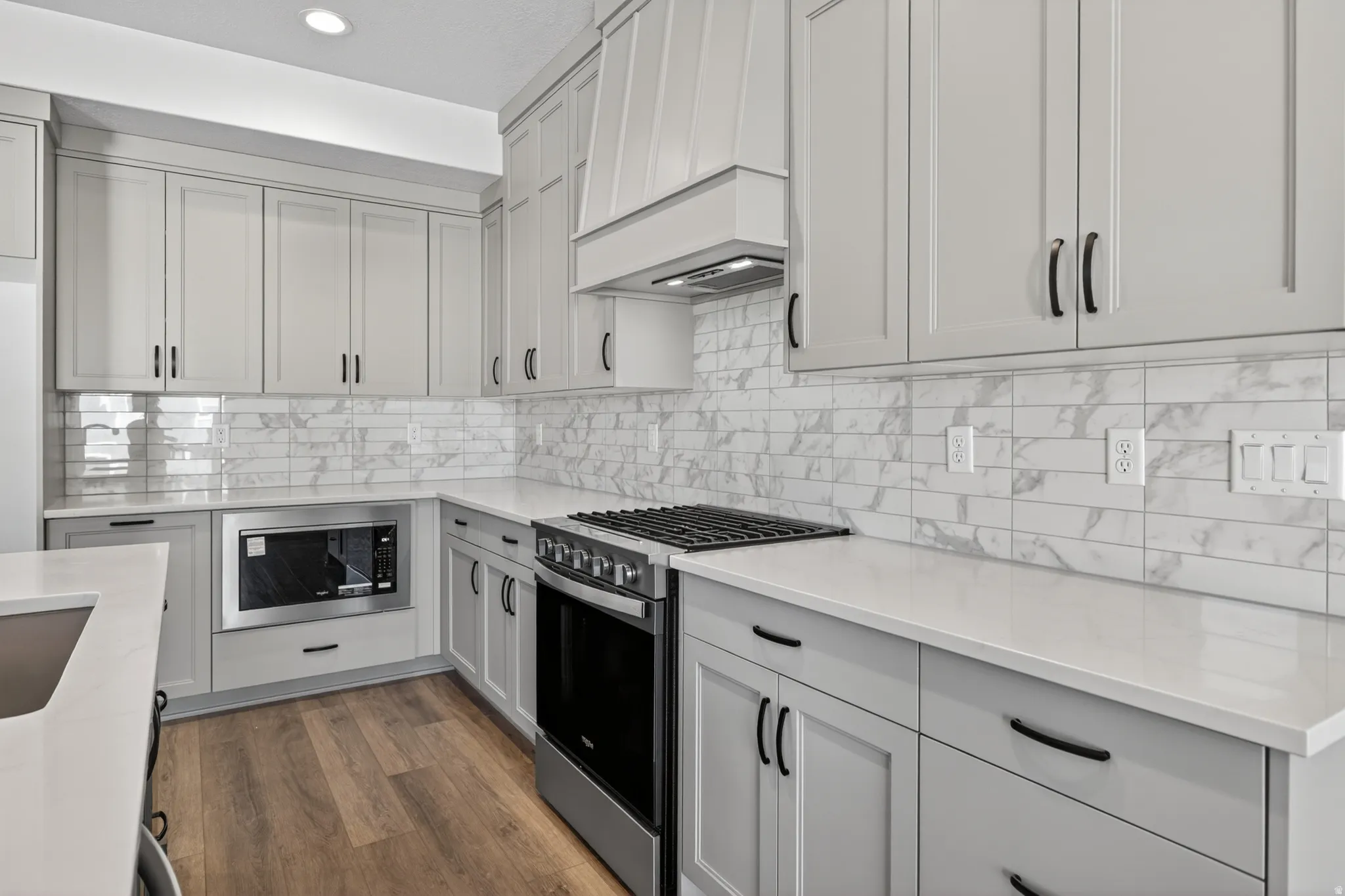 Modern kitchen featuring light gray shaker-style cabinetry, white countertops, and wood-finish flooring