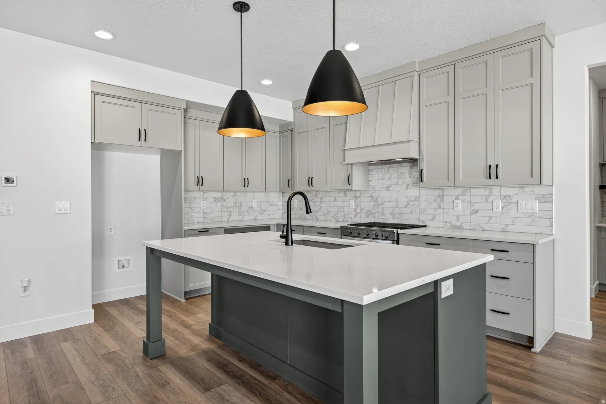 Modern kitchen featuring a central island with a white countertop and dark gray base, complemented by two contemporary pendant lights
